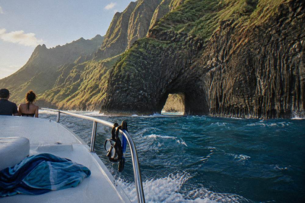 Small boat near tall sea cliffs with a stone arch at the waterline