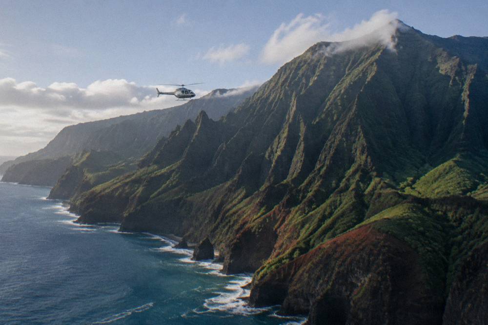 Helicopter flying above a coastline of ridges and deep green valleys