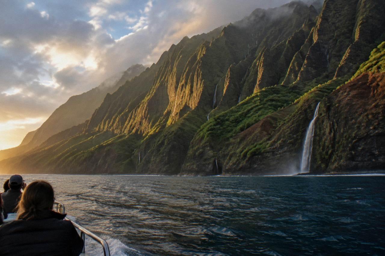 Sea cliffs rising from the ocean along a rugged green coastline with waterfalls
