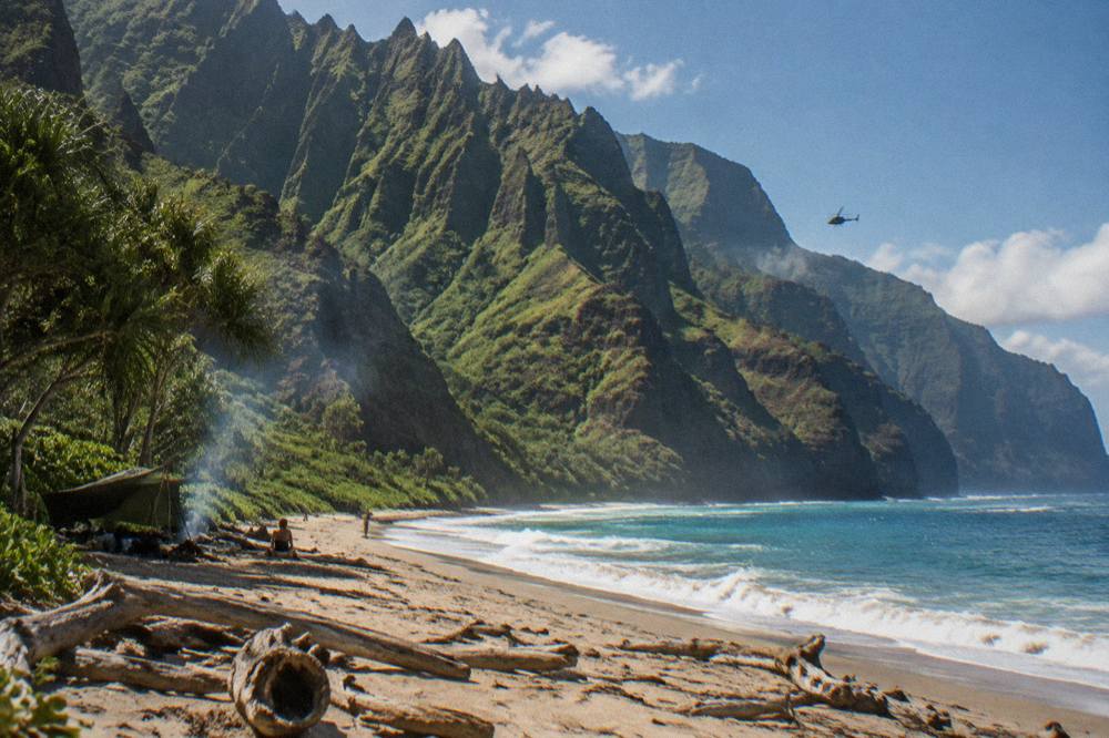 Private helicopter hovering above the Na Pali Coast with sheer emerald cliffs and deep blue water