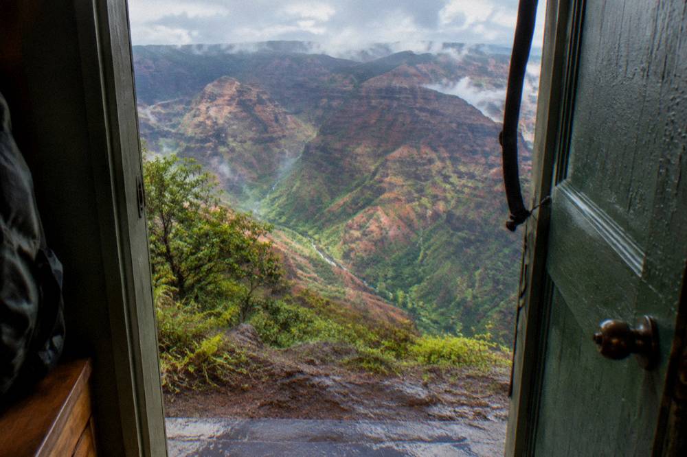 Aerial view of Waimea Canyon's red and green layered cliffs from a doors-off helicopter