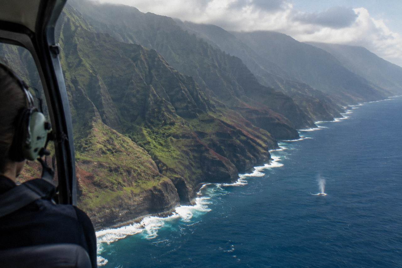 Private helicopter flying over the Na Pali Coast with dramatic green cliffs and blue ocean below
