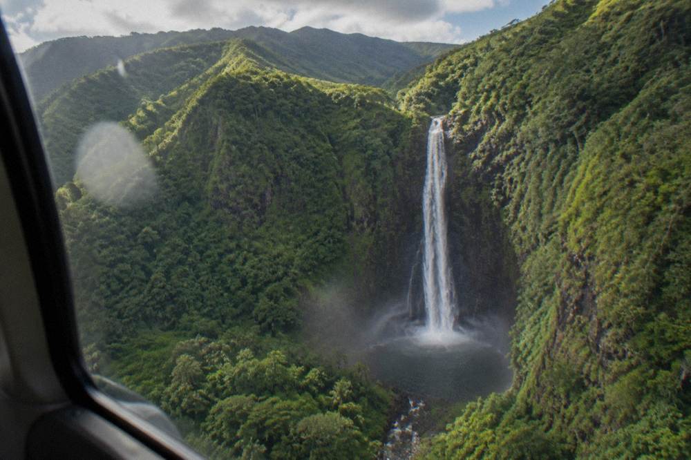 Waterfall dropping into a narrow green canyon valley with mist rising