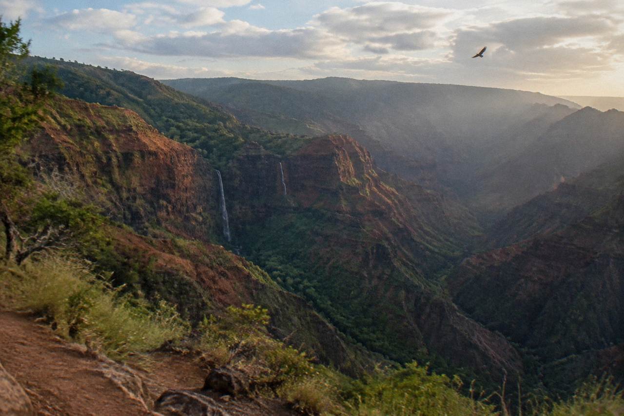 Aerial view of deep red and green canyon walls with thin waterfalls dropping into the gorge