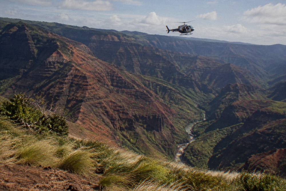 A helicopter flying above a deep canyon with red walls and a river channel far below