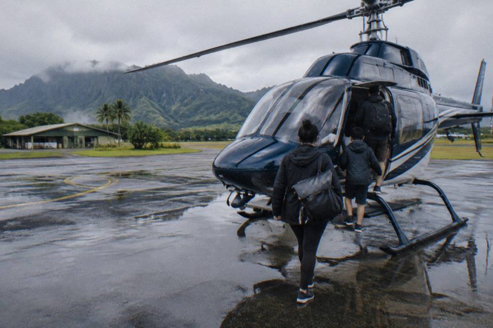 A family in dark layered clothing boarding a helicopter at a Lihue heliport