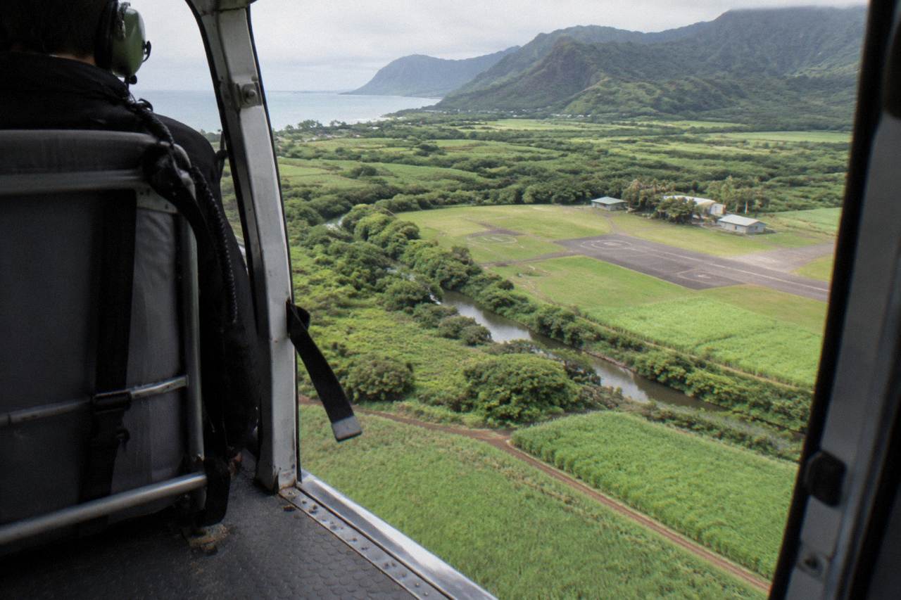 A helicopter cabin interior above green Kauai valleys seen through the open door frame